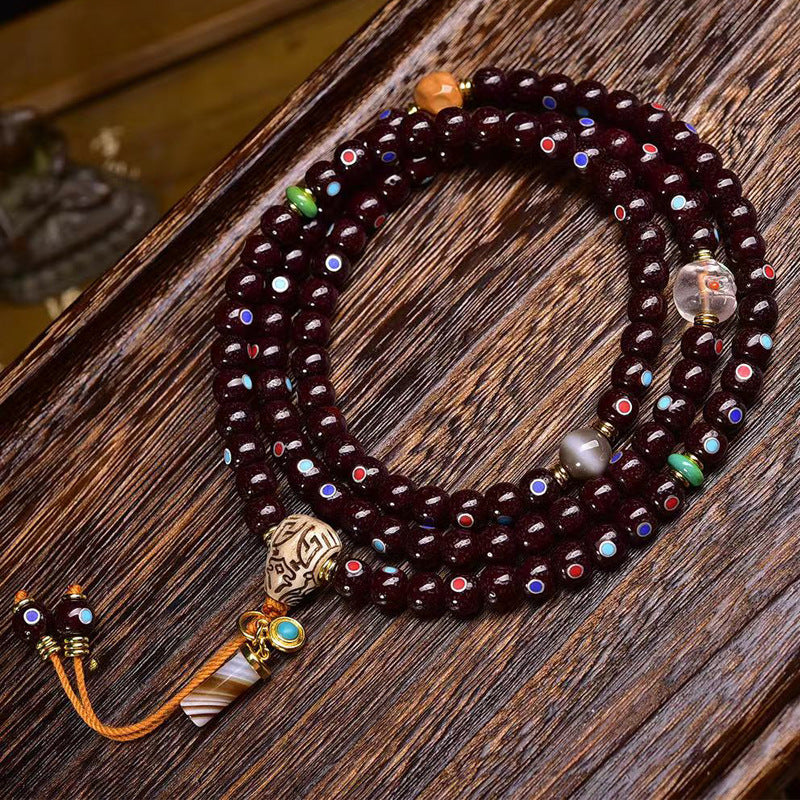 Natural Cinnabar Star Seed Bodhi Mala — 108 bead meditation bracelet with colorful accents on a wooden surface.