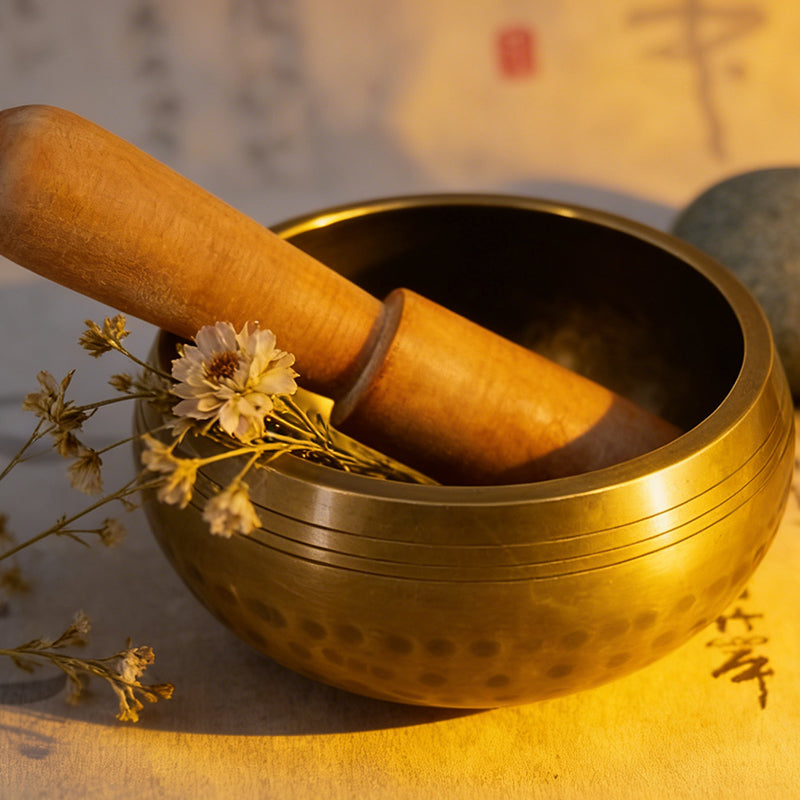 Nepalese hammered singing bowl with wooden mallet and decorative flowers for sound healing and meditation.